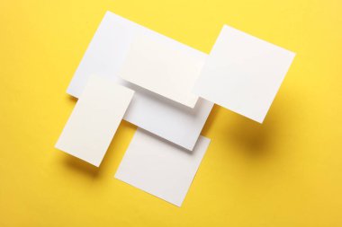 Sarı zemin üzerinde yüzen beyaz kare not kağıdı ve kartların bileşimi. Modelleme. İş konsepti