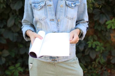 Kot ceketli bir kadın yeşil bitki arka planında boş şarjör tutuyor.