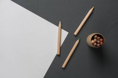 Ahşap renkli kalemlerle dolu bir kutu ve koyu gri arka planda kağıt çarşaf. Yaratıcılık, sanat. Üst görünüm