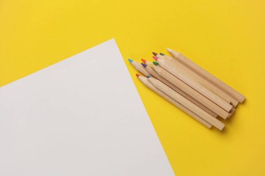 Tahta renkli kalemler ve sarı arka planda kağıt çarşaf. Yaratıcılık, sanat