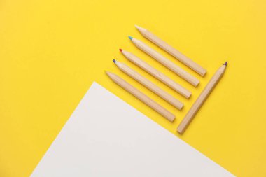 Tahta renkli kalemler ve sarı arka planda kağıt çarşaf. Yaratıcılık, sanat