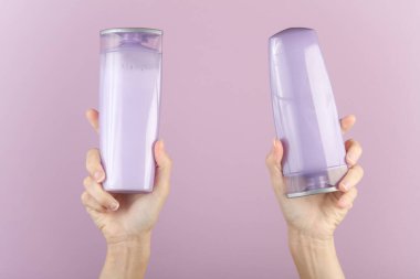 Mor pastel arka planda şampuan şişeleri tutan kadın eller.