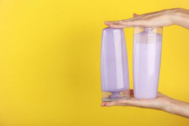 Sarı arka planda şampuan şişeleri tutan kadın eller.