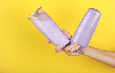 Sarı arka planda şampuan şişeleri tutan kadın eller.