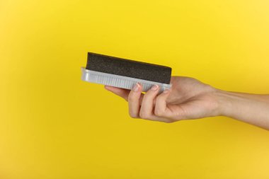 Sarı arka planda süet ayakkabıları temizlemek için bir sünger tutuyorum.