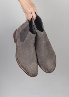 Elinde gri bir arka planda Chelsea marka süet botlar var.