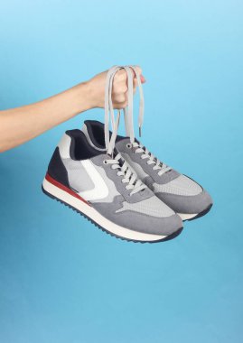 Mavi arka plandaki bağcıklardan gri spor ayakkabıları tutarken