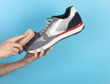 Eller mavi arka planda spor ayakkabılarını fırçalıyor