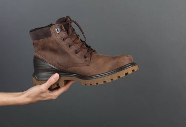 Koyu gri bir arka planda, kışlık deri bir bot tutuyor.