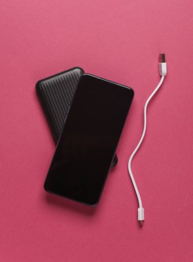 Siyah güç bankası ve pembe arka planda akıllı telefon.
