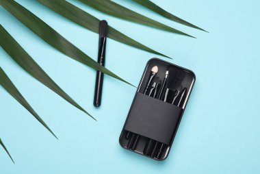 Mavi arka planda yeşil palmiye yaprağı olan makyaj fırçası seti. Güzelliğin ve modanın yaratıcı düzeni natürmort hayat