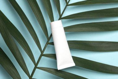Mavi arka planda yeşil palmiye yaprağı olan beyaz krema tüpü. Güzelliğin ve modanın yaratıcı düzeni natürmort hayat