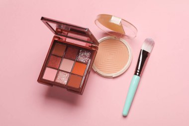 Göz farı paleti, pudra pudrası ve pembe arka planda makyaj fırçası.