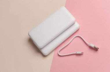 Pastel arka planda kablolu beyaz güç bankaları. Akıllı telefon ve diğer cihazları şarj etmek için harici bataryalar. Üst görünüm