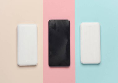 Pastel arka planda akıllı telefonu olan beyaz güç bankaları. Akıllı telefon ve diğer cihazları şarj etmek için harici bataryalar.