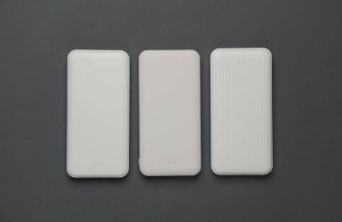 Koyu gri arka planda kablolu beyaz güç bankaları. Akıllı telefon ve diğer cihazları şarj etmek için harici bataryalar. Üst görünüm