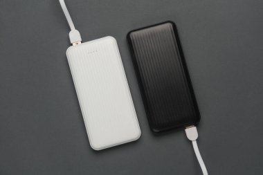 Koyu gri arka planda kablolu elektrik bankaları. Akıllı telefon ve diğer cihazları şarj etmek için harici bataryalar. Üst görünüm