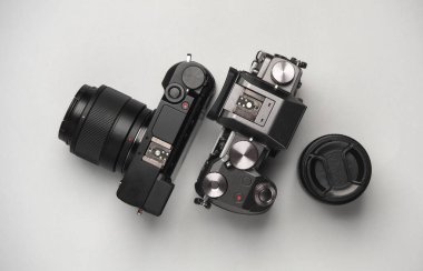 Gri arka planda lensleri olan iki modern dijital aynasız kamera. Üst görünüm