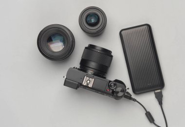 Gri arka planda elektrik bankasından gelen mercekleri olan modern dijital aynasız kamera. Üst görünüm