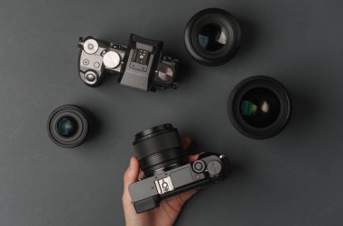 Eller koyu gri arka planda lensleri olan modern aynasız kamerayı tutuyor. Fotoğraf ekipmanı.