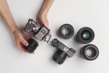 Eller, beyaz arka planda lensleri olan modern aynasız kamerayı tutuyor. Fotoğraf ekipmanı.