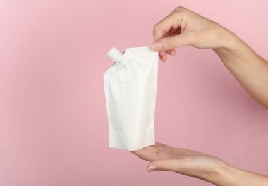 Pembe arka planda şeker kutusuyla beyaz bebek çantası tutan eller. Tasarım için şablon, model