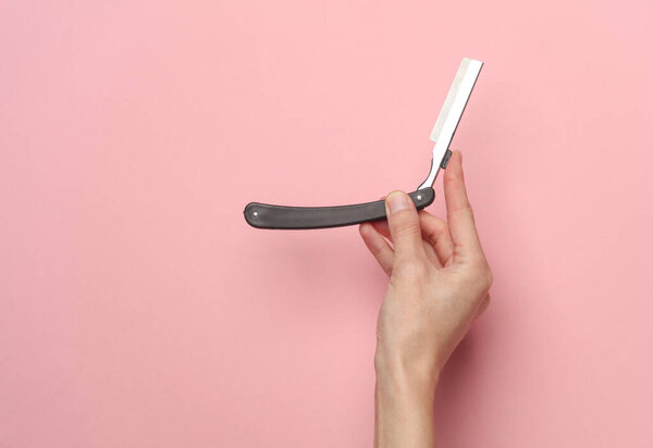 Hand holding a straight razor on a pink background