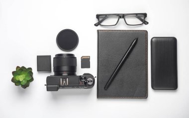 Kamera, not defteri ve beyaz arka planda aksesuarları olan yaratıcı bir düzen. Düz yatıyordu