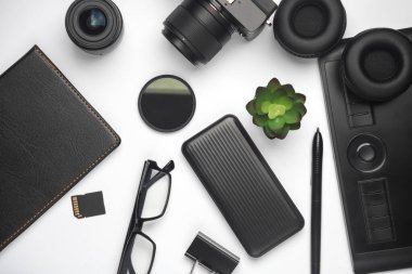 Kamera, tablet, güç bankası, kulaklık ve beyaz üzerine not defteri. Modern aksesuarlar ve aletler. Bir fotoğrafçının ya da rötuşçunun çalışma ekipmanları. Düz yatıyordu. Üst görünüm