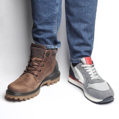 Beyaz arka planda farklı ayakkabılar giyen erkek bacakları.