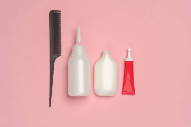 Saç boyamak için tüpler ve pembe pastel arka planda taraklar