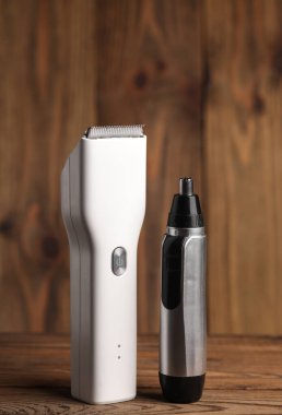 Beyaz, modern, kablosuz saç makası ve tahta arka planda burun kesicisi.