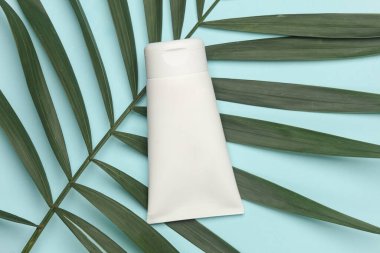 Mavi arka planda, palmiye yapraklı krema tüpü.