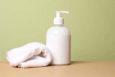 Yeşil arka planda bir şişe duş jeli ve havlu.