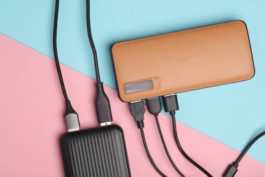 Pembe arka planda birçok USB kablosu olan iki dış güç bankası bataryası. Üst görünüm
