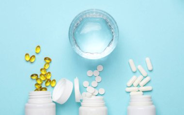 Plastik şişelerde farklı haplar ve mavi arka planda su bardağı. Tıp konsepti. Üst görünüm