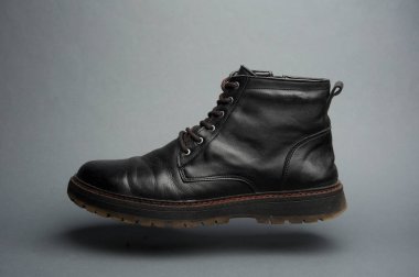 Koyu gri arka planda yüzen siyah deri erkek çizmesi.