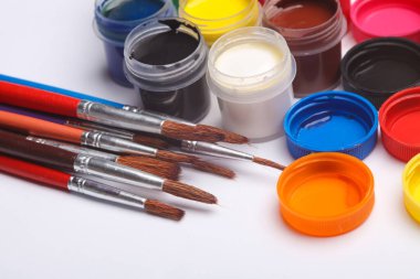 Beyaz arka planda fırçalarla şişelere boyanmış guaj tabloları. Çocukların yaratıcılığı