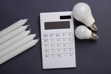 Alternatif aydınlatma, tasarruf. Koyu arkaplanda lamba ve mum bulunan hesap makinesi
