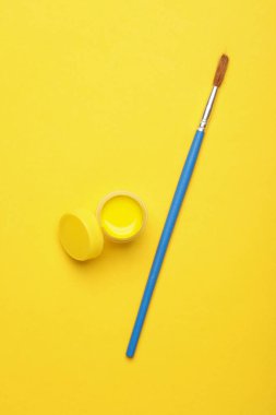 Sarı gouache boya kavanozu ve sarı arka planda fırça.
