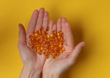 Sarı arka planda balık yağı kapsülleri.