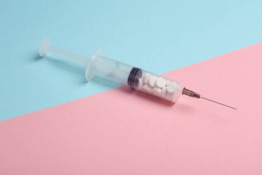 Şırınga mavi pembe arka planda haplarla dolu. Sağlık ve Tıp Konsepti