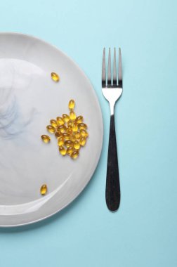 Tabakta balık yağı kapsülleri ve mavi arka planda çatal. Diyet, sağlıklı yemek.