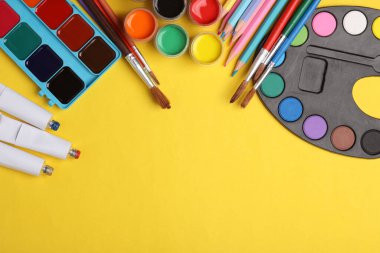 Sarı arka planda boya, renkli kalemler ve fırçalar. Yaratıcılık için ürünler. Boşluğu kopyala