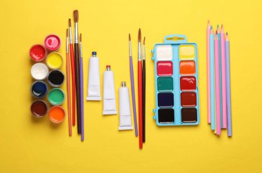 Sarı arka planda boya, renkli kalemler ve fırçalar. Yaratıcılık için ürünler