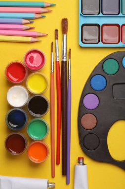 Sarı arka planda boya, renkli kalemler ve fırçalar. Yaratıcılık için ürünler