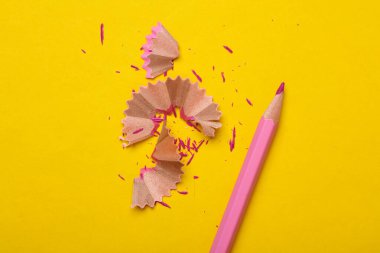 Keskinleştirilmiş pembe renkli kalem, sarı arka planda talaşı var.