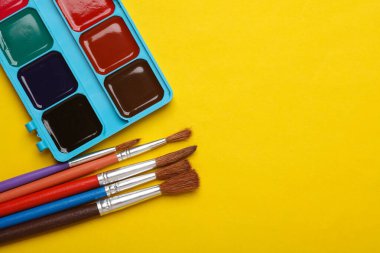 Sarı arkaplanda fırçalar olan suluboya palet