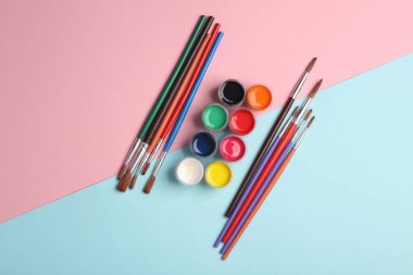 Mavi-pembe arka planda, şişe ve fırçalarla yapılmış guaj boyası seti.