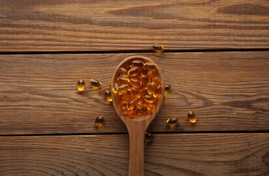 Tahta bir masada tahta kaşıkta balık yağı kapsülleri..